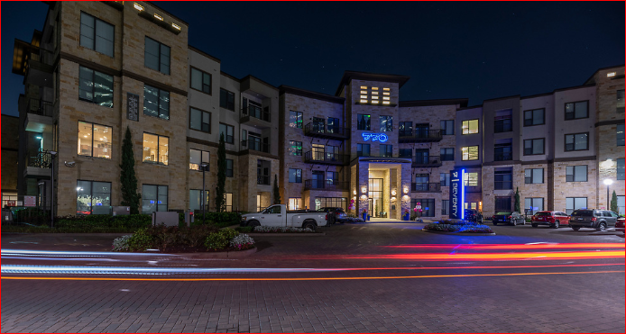 a city street at night with cars parked in front of an apartment building