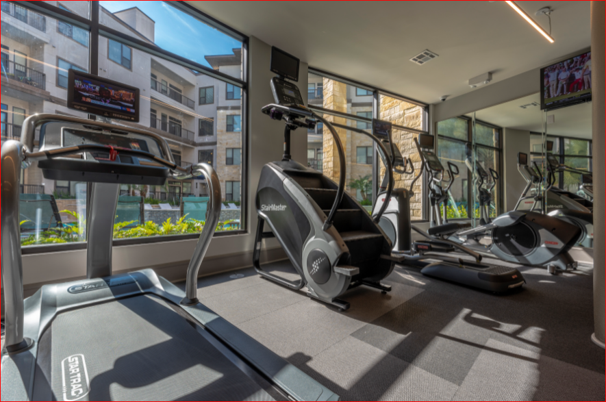 a gym with cardio equipment and a window overlooking a city street