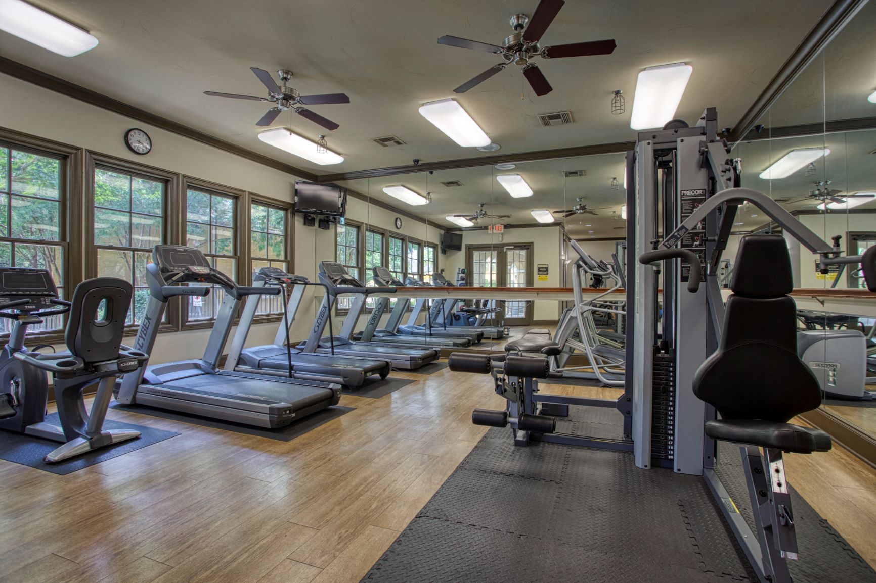 a gym with cardio machines and weights on the floor and windows