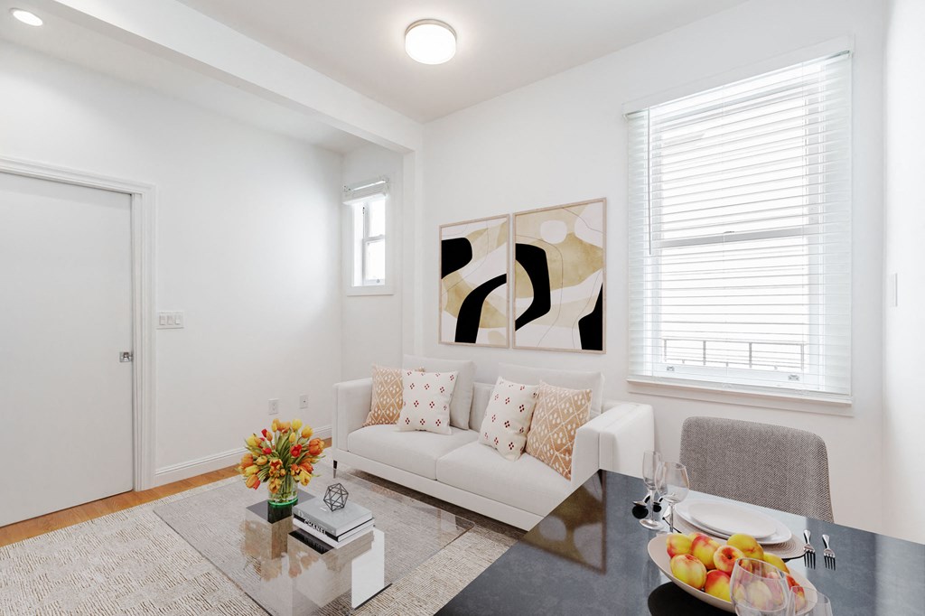 A modern living room with a white couch, a coffee table with a vase of flowers, and a painting on the wall.