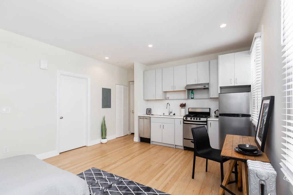 a living room with a table and a kitchen with white cabinets