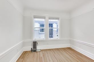 an empty room with white walls and wooden floors and two windows