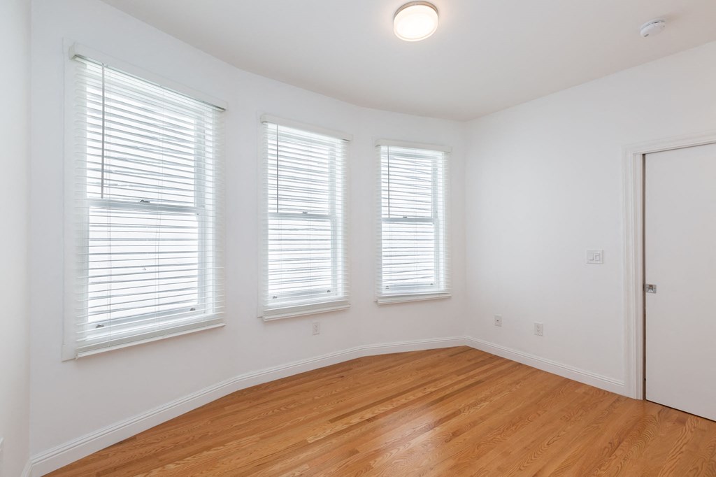 A room with wooden floors and two windows with blinds.