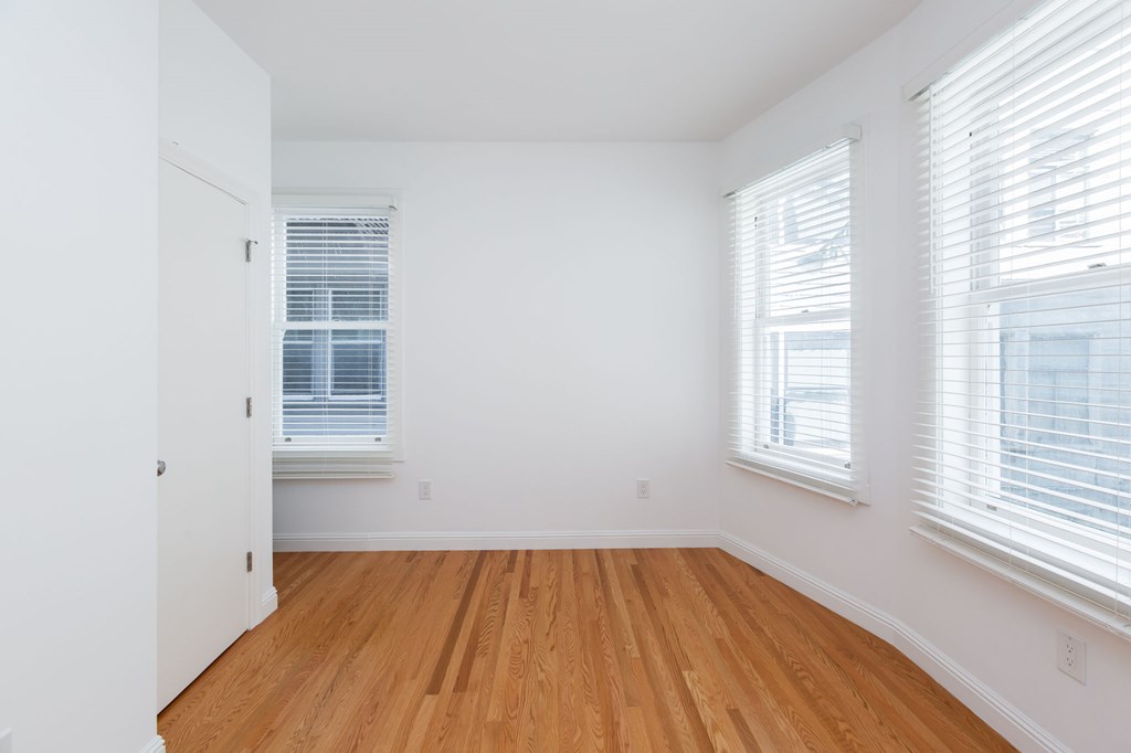 A room with wooden floors and two windows with blinds.