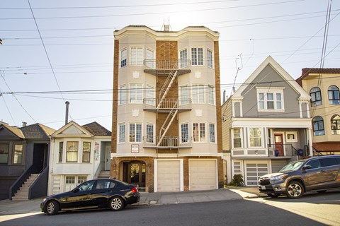 A black car is parked in front of a two-story building with a garage.
