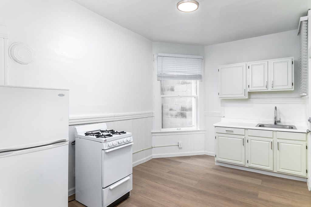 A white kitchen with a stove, sink, and cabinets.