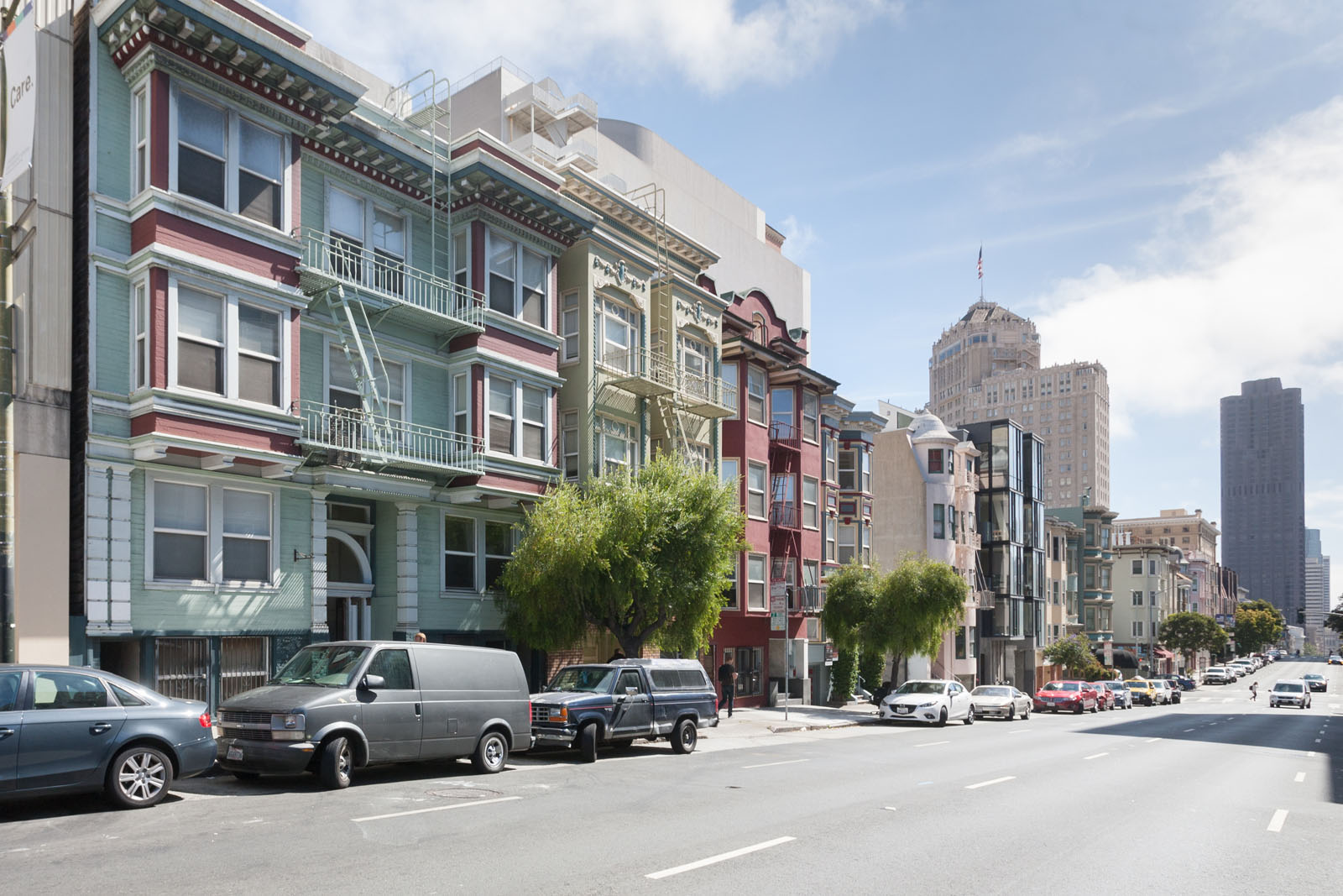 A row of colorful buildings line a street with cars parked on the side.