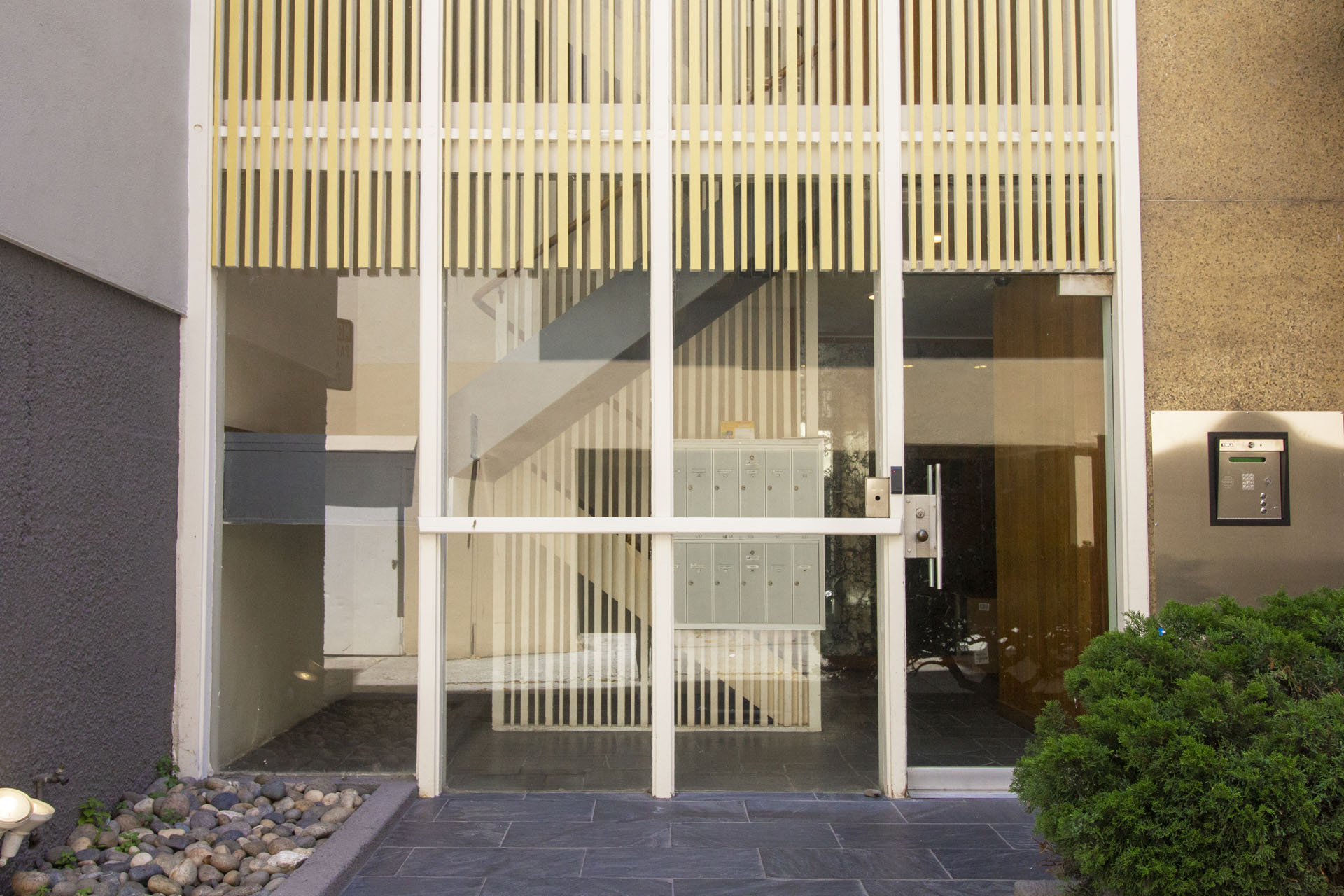 A modern house entrance with a glass door and a wooden slatted awning.