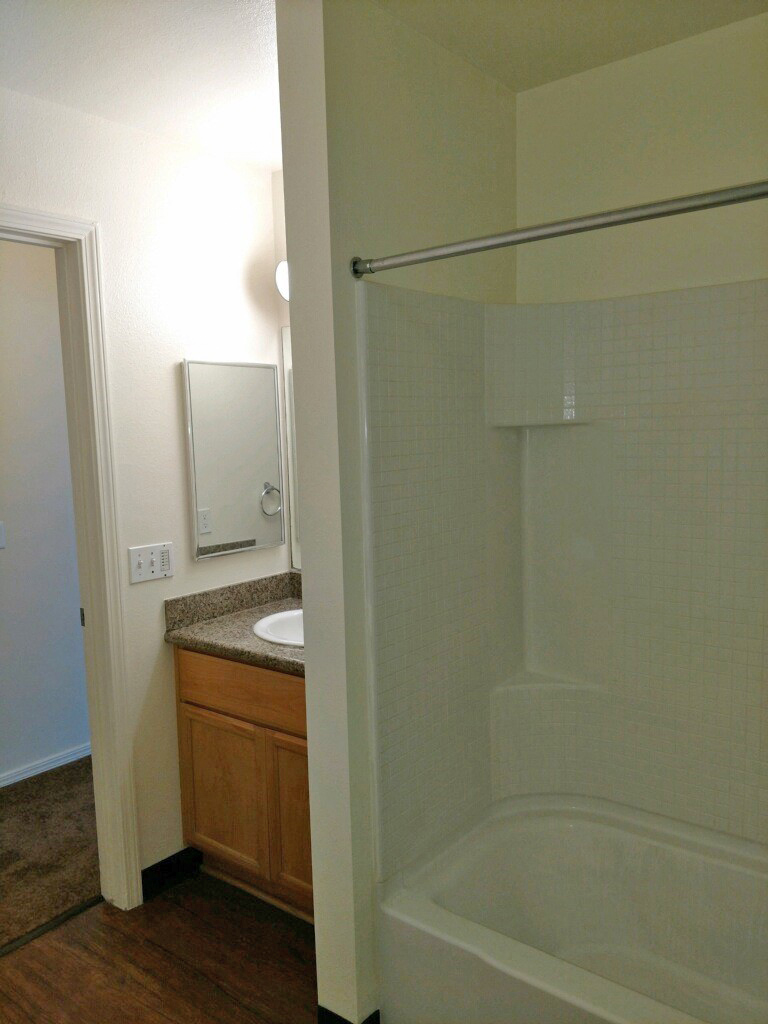 Main bathroom showing tub, shower curtain bar and sink with overhead lights and mirrors.  Flooring is woodgrain vinal.