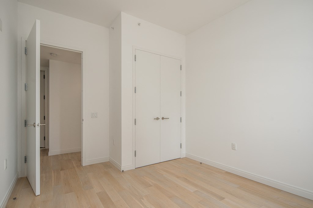 a bedroom with white walls and wooden floors and a closet