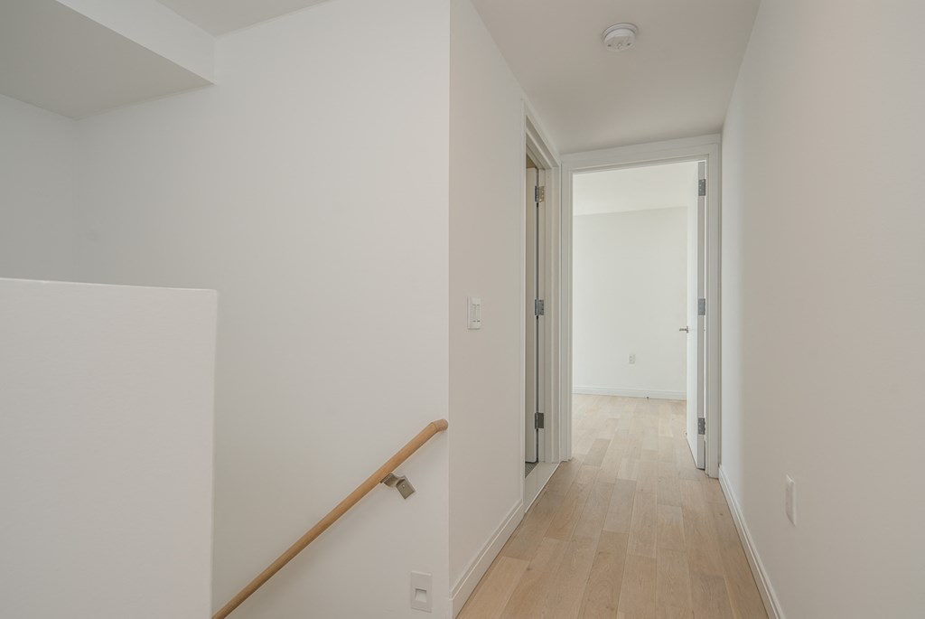 a hallway in a home with white walls and wood flooring