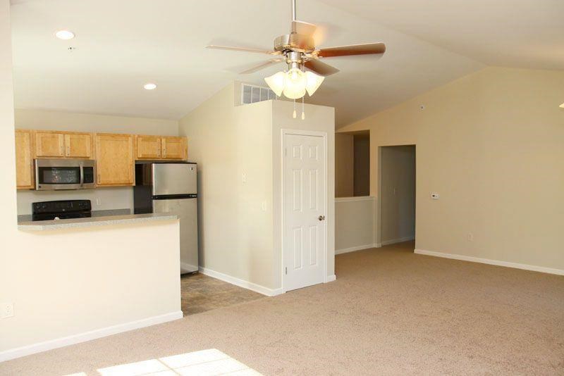 an empty living room with a kitchen and a ceiling fan