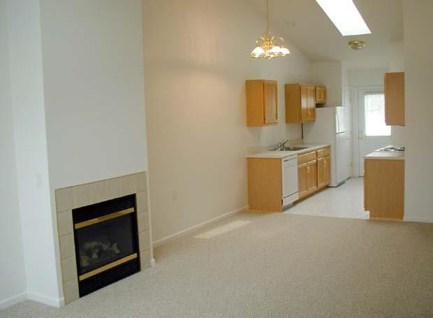 an empty living room with a fireplace and a kitchen