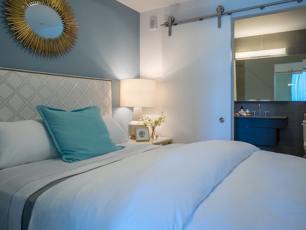 a white bed with a blue pillow and a mirror above it