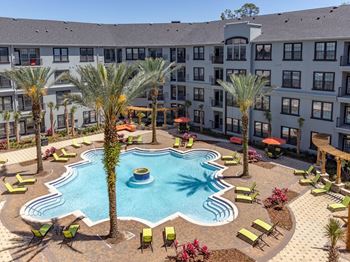 Large Swimming Pool surrounded by four palm trees, plenty of sunning chairs at The Bartram Apartments in Gainesville, FL