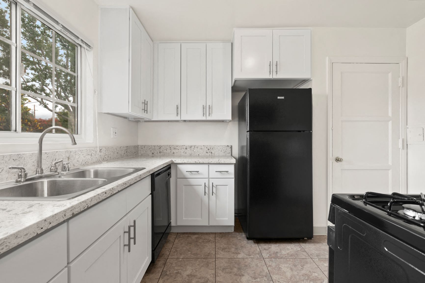 Van Nuys Apartments for Rent - Colonial Manor Modern Kitchen with Black Appliances, White Cabinetry, and Large Window