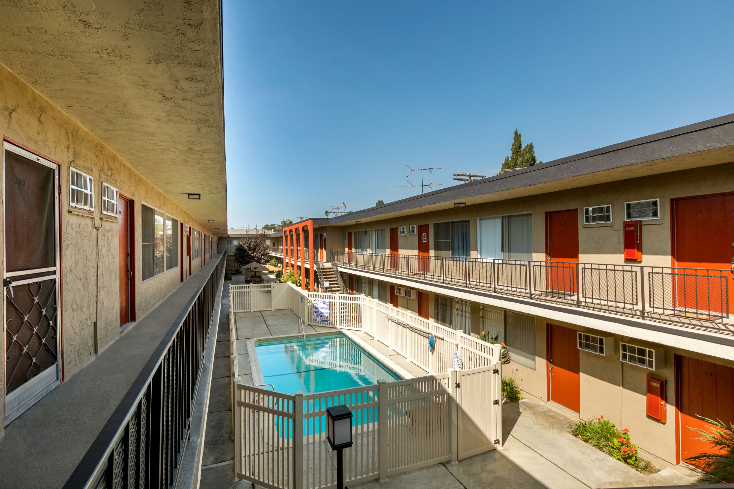 Apartments in Valley Village CA - Riverside Villa - Tan Building Exterior with View of Blue Pool and Poolside Area