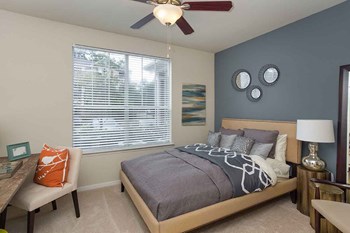 Apartments for Rent in The Woodlands TX - Whispering Pines Ranch - Furnished Bedroom With Comfortable Bed, a Ceiling Fan, and a Desk With a Chair on Top of Carpet Flooring - Photo Gallery 15