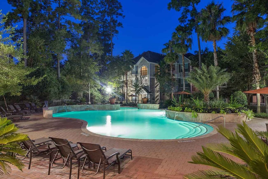 a large swimming pool with chairs around it at night