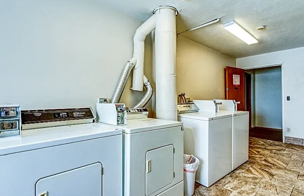 three washers and dryers in a laundry room with a pipe