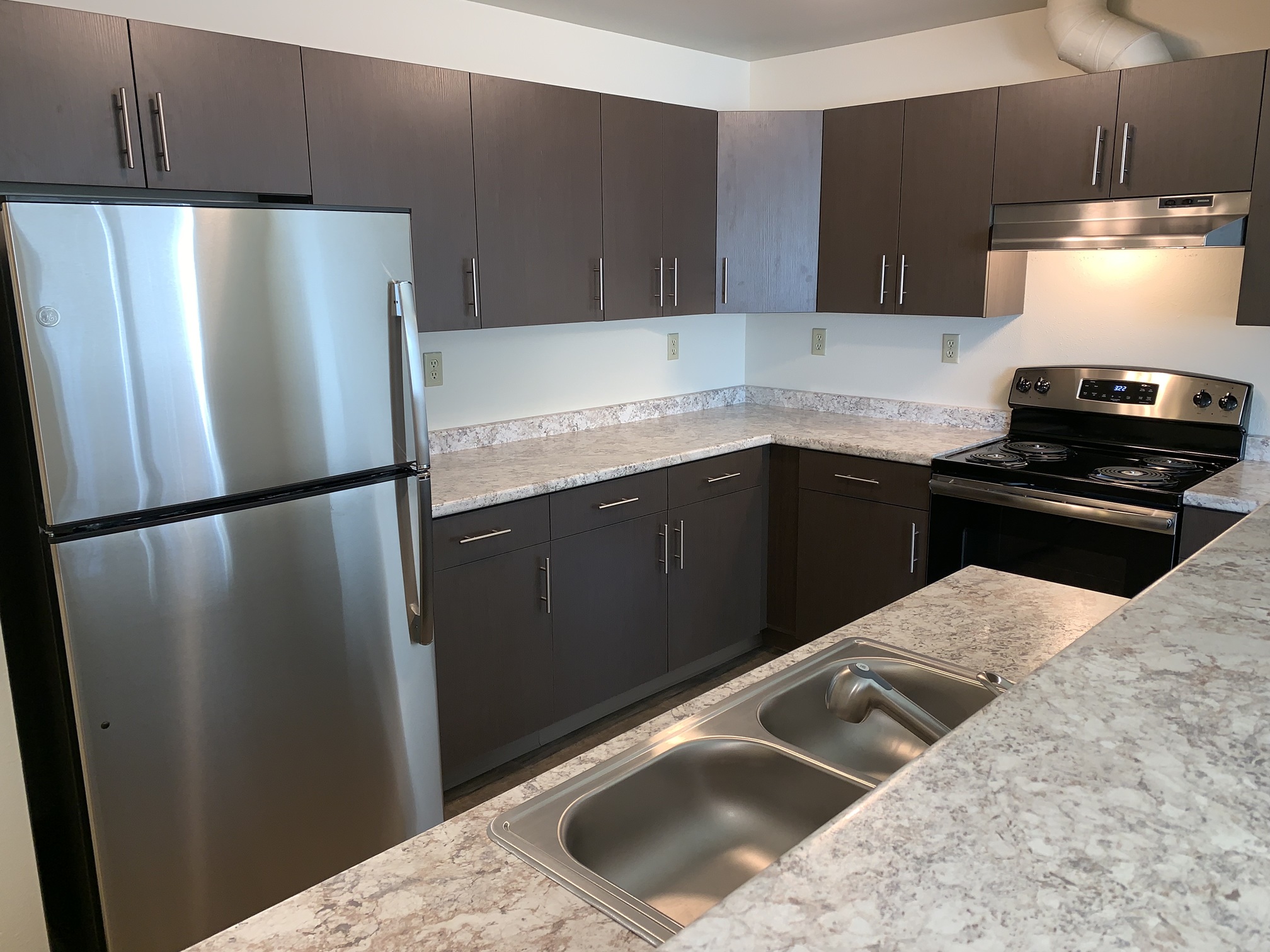 A kitchen with a stainless steel refrigerator and a marble countertop.