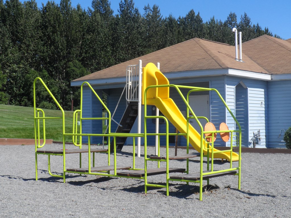 a playground with a yellow slide in front of a blue building
