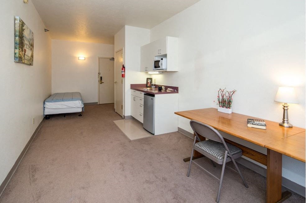 a room with a desk and a kitchen and a bed