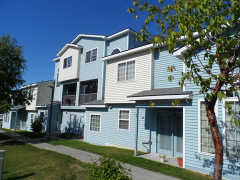 A blue and white two story apartment building with a tree in front.