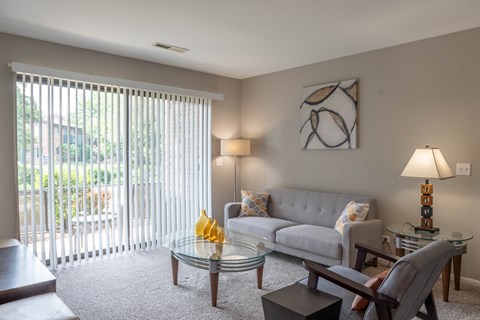 A living room with a grey couch, a glass table, and a painting on the wall.