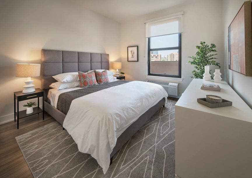A bedroom with a large bed and a window overlooking a cityscape.