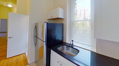 A black fridge in a kitchen with white cabinets and a wooden floor.