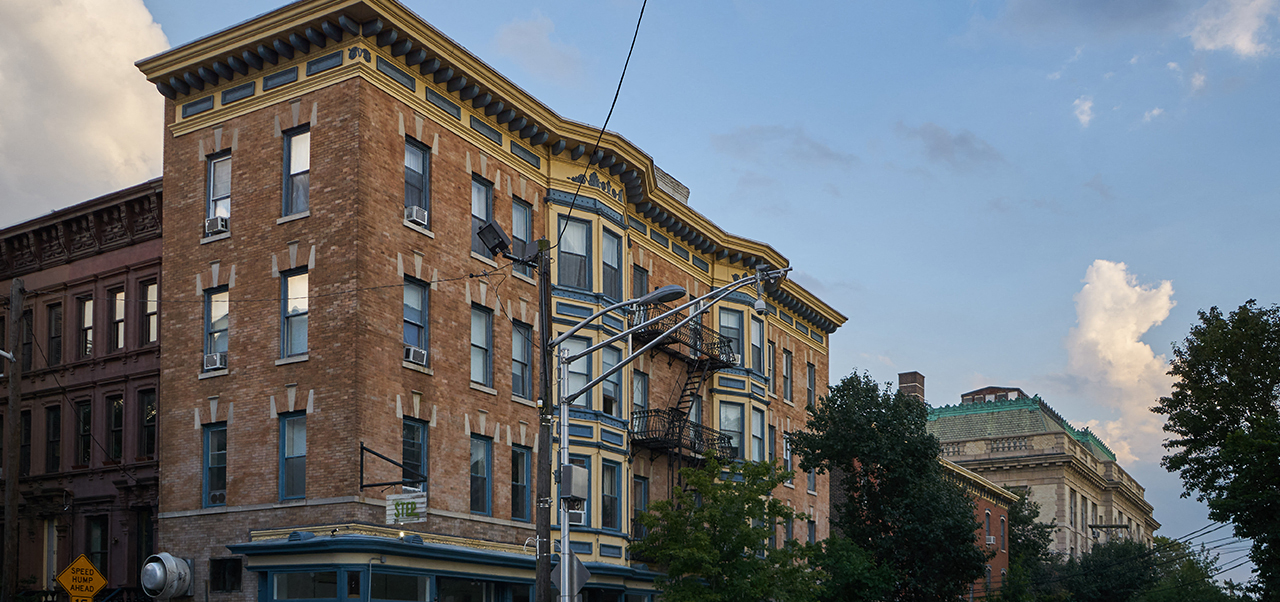 A tall brick building with a yellow trim and a green roof.