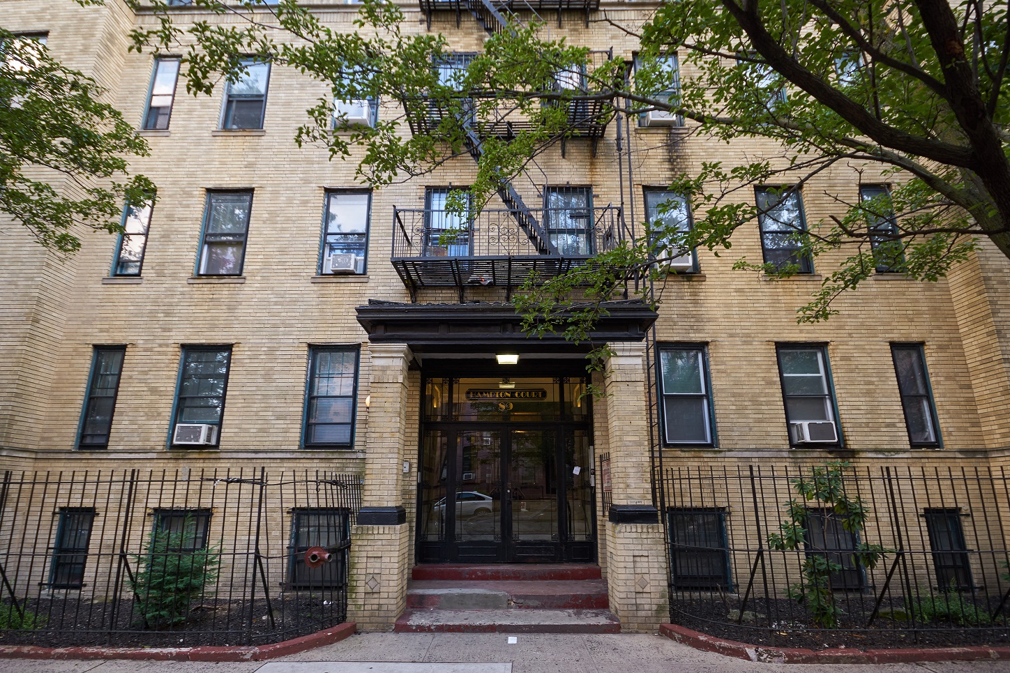 A building with a black iron fence and a tree in front.