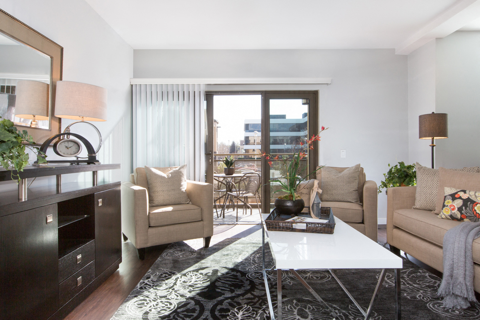 Apartments near Santana Row in Cupertino, CA - Nineteen800 - Livingroom with Hardwood-Style Floor, Area Rug, Sofa, Two Armchairs, Coffeetable, Cabinet, Lamps, Decorative Mirror, and Door with Access to Private Balcony
