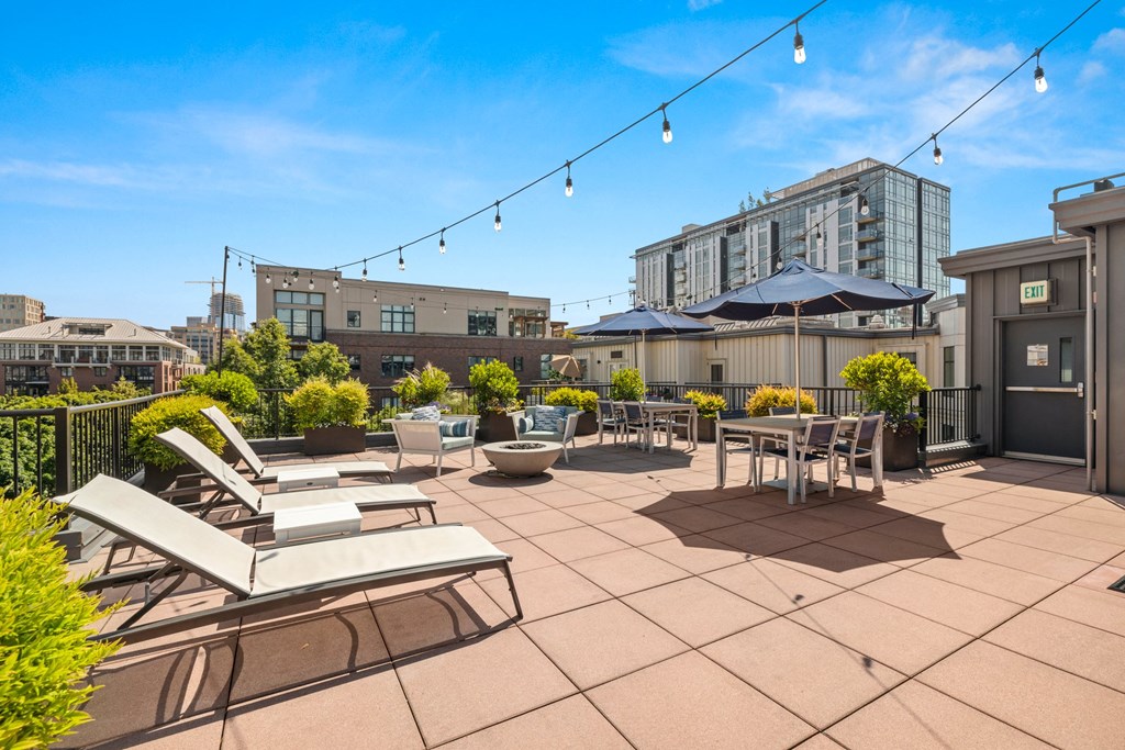 a rooftop patio with chairs tables and umbrellas and buildings in the background