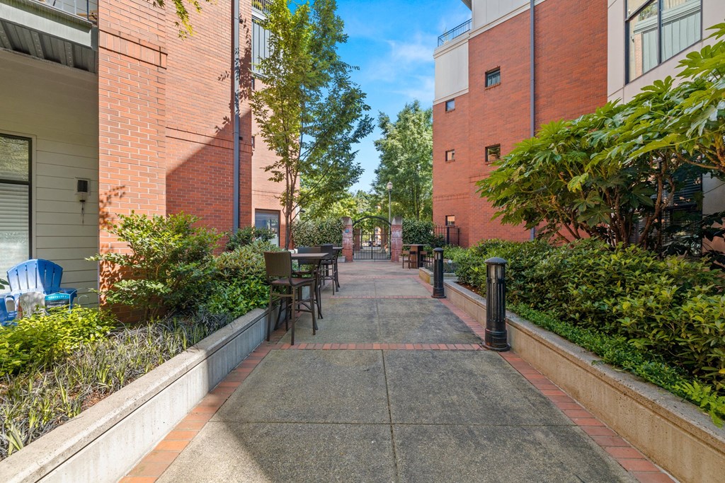 an empty sidewalk between two buildings with tables and chairs on the side