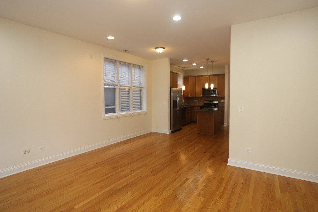 an empty living room with wood floors and a kitchen