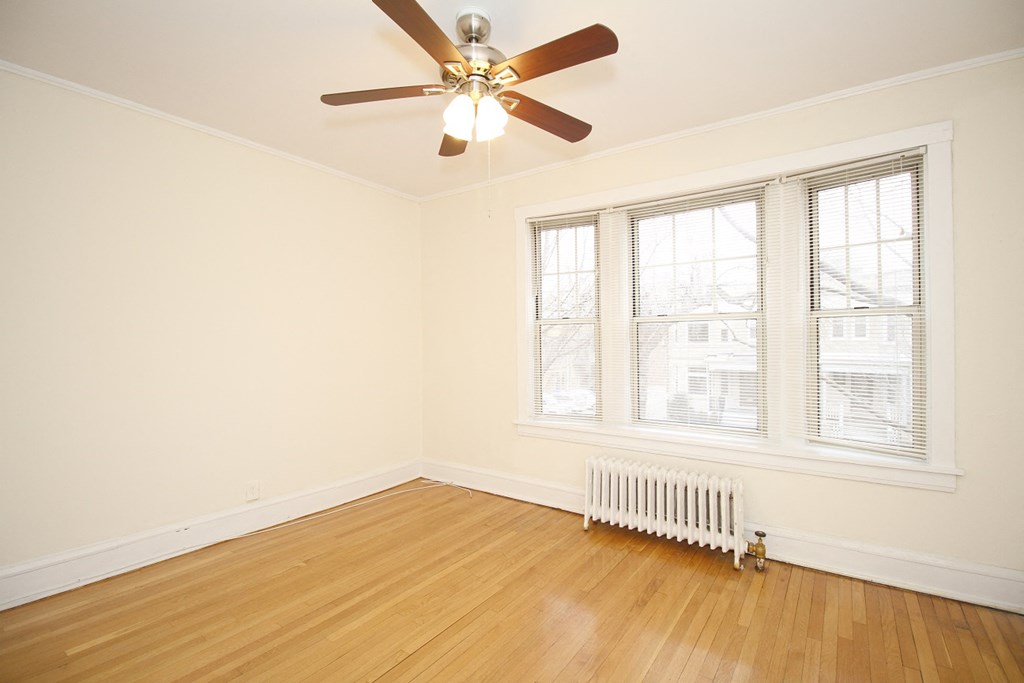 an empty living room with a ceiling fan and a radiator