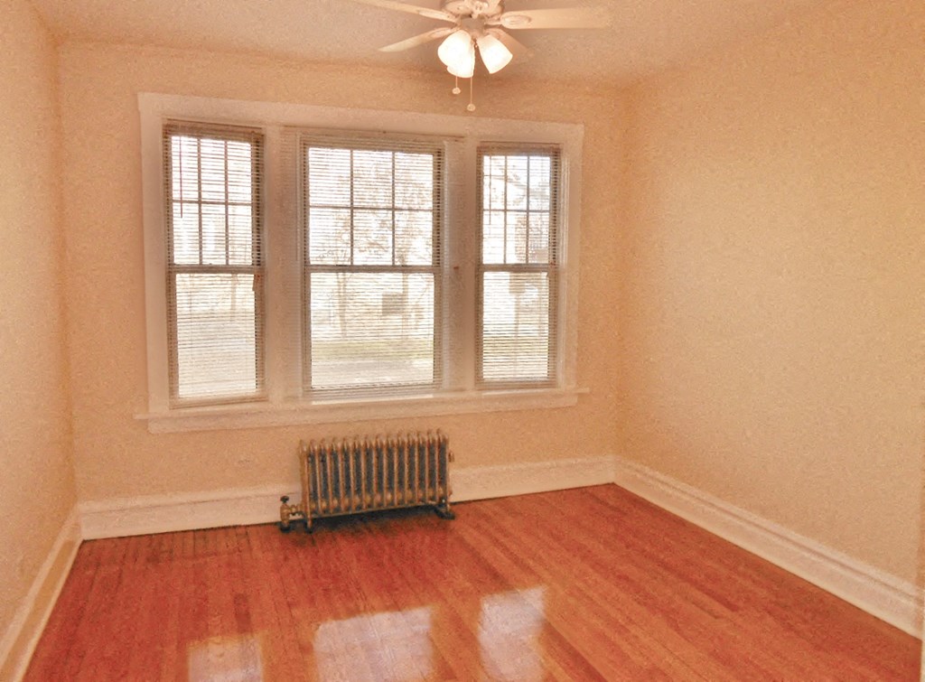 a living room with a wooden floor and a radiator in front of three windows