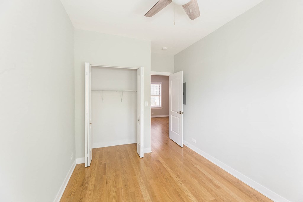 a bedroom with white walls and wood floors and a closet