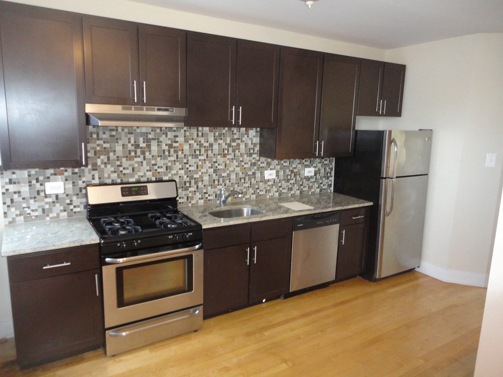 an empty kitchen with wooden floors and stainless steel appliances