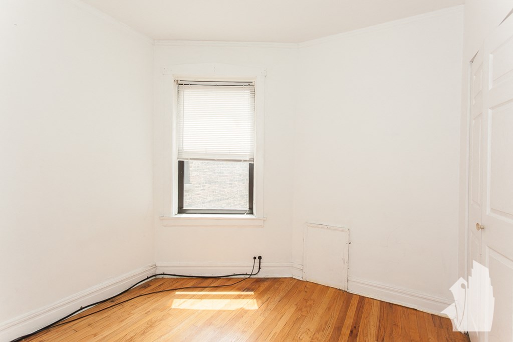 a room with white walls and a window and wood floors