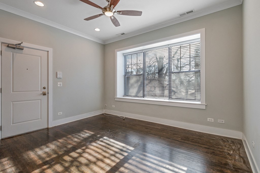 an empty living room with a large window and a ceiling fan