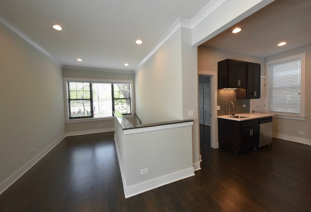 an empty living room with a kitchen and a window