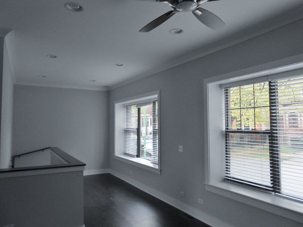 an empty room with two windows and a ceiling fan