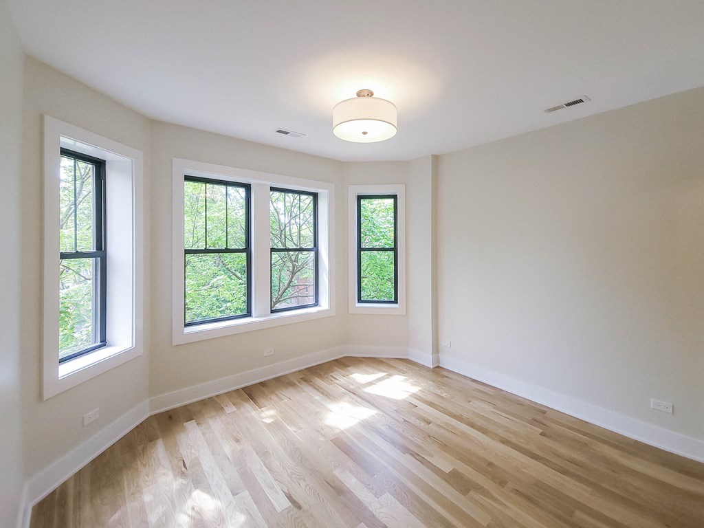 an empty living room with a hardwood floor and three windows