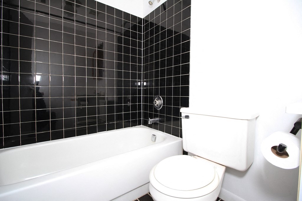 a bathroom with black tile and a white toilet and tub