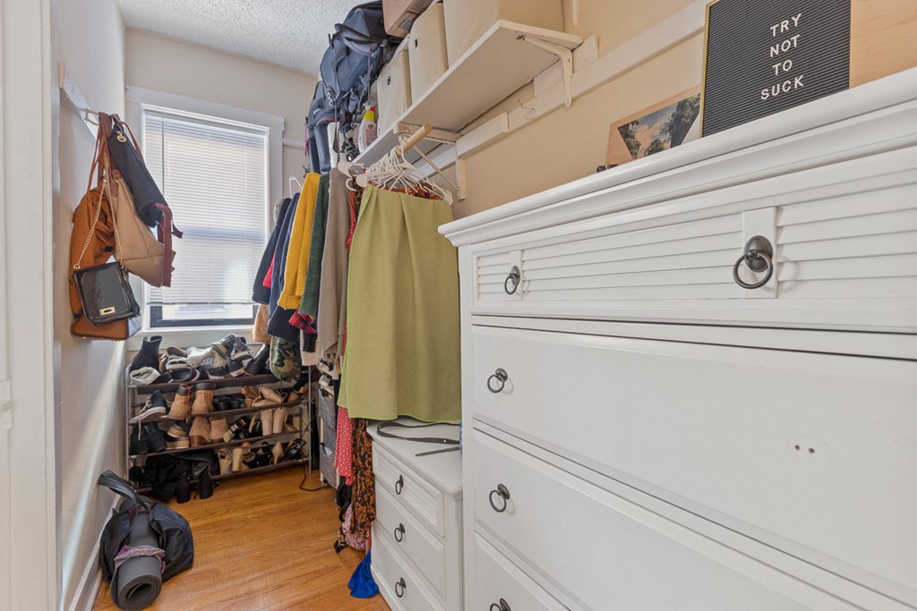a walk in closet with a dresser and clothes hanging in it