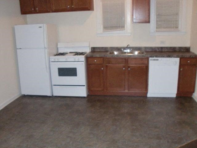 an empty kitchen with white appliances and a sink