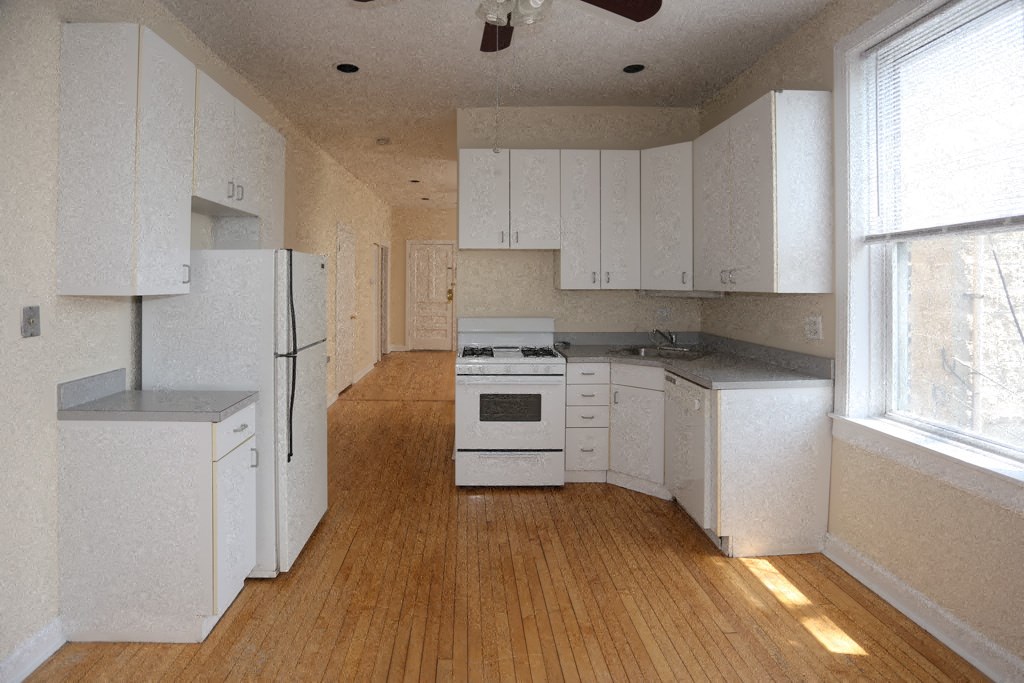 an empty kitchen with white cabinets and a refrigerator